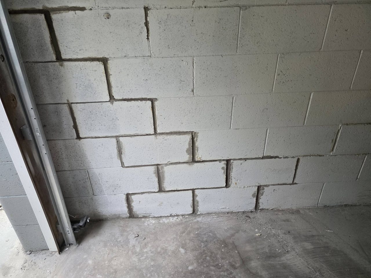 Interior concrete-block (CMU) basement wall showing mortar joints and a metal door frame on the left side.